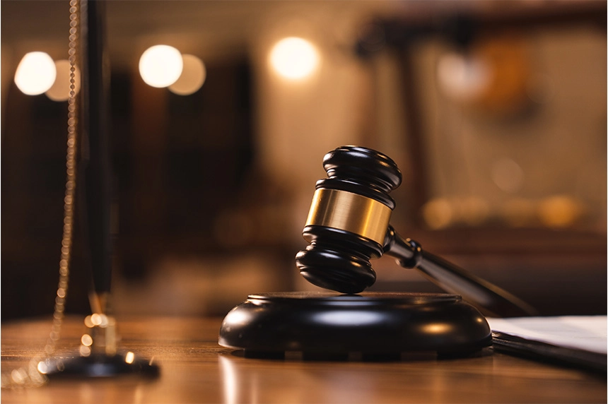 A close-up image of a gavel on a wooden block in a courtroom, with a blurred background.