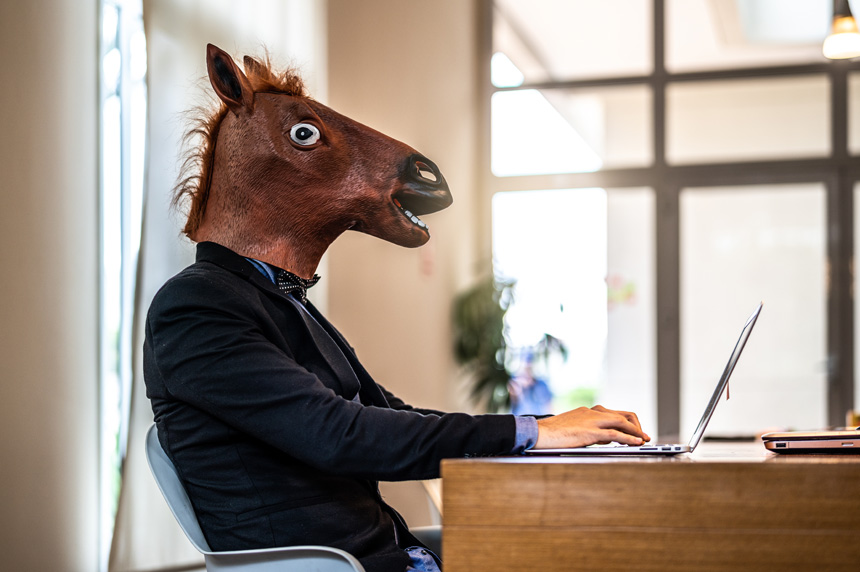 Person wearing horse mask sitting at their laptop
