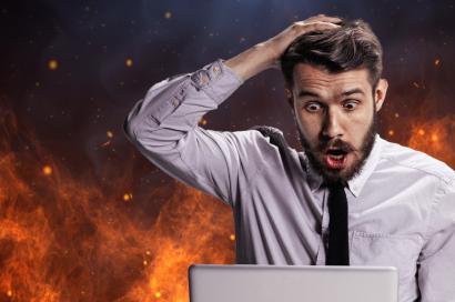 man with shocked face looking at laptop with fire in background